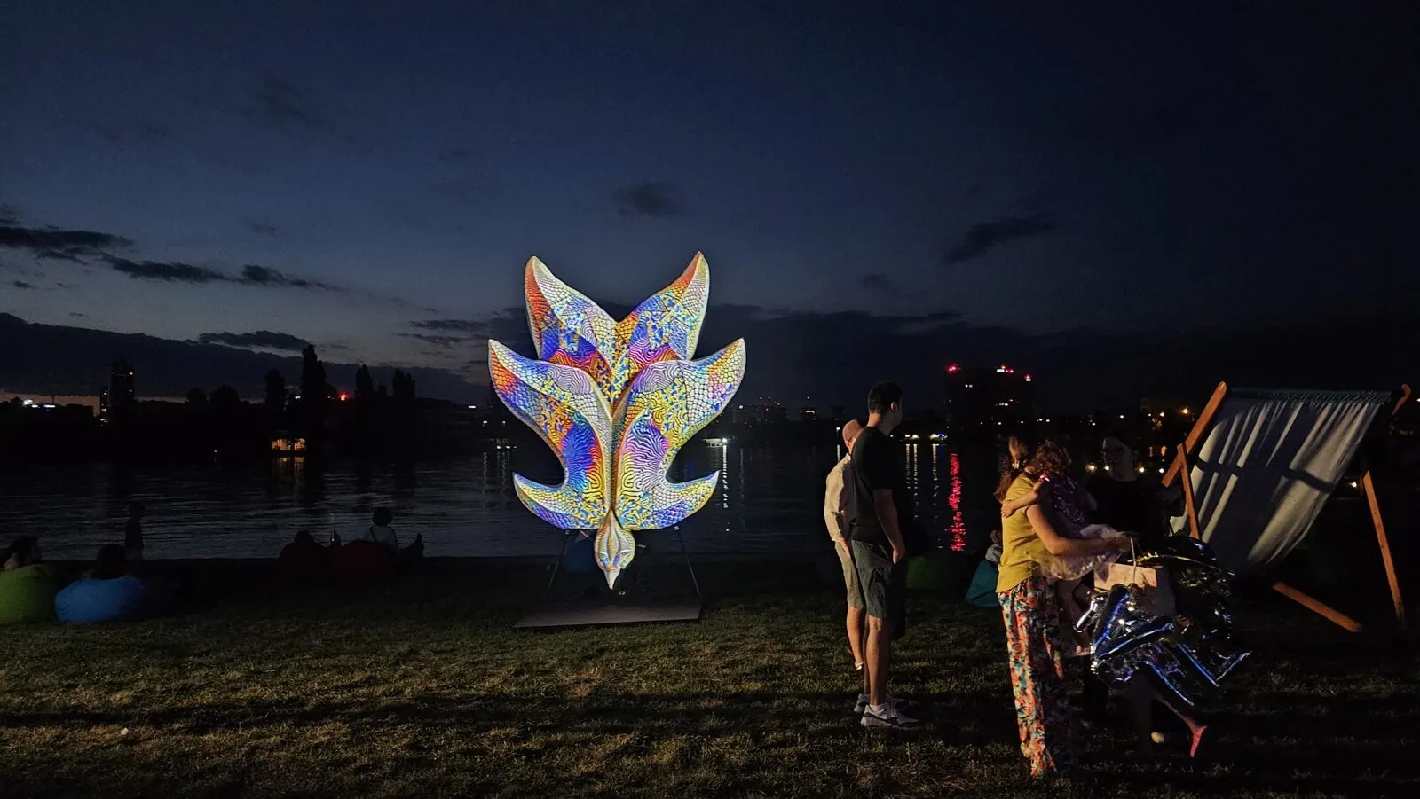 Forme care tac / Forme care luminează — instalație pe malul lacului, cu skyline-ul orașului